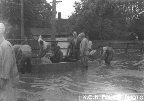 Boat - A motorboat proved to be a very practical way to get around in the Armourdale community during the 1951 flood. Harold Smith, a powerboat dealer (center of photo wearing cap) is seen near Seventh Street and Kansas Avenue. (Photo courtesy of Wyandotte County Museum) 