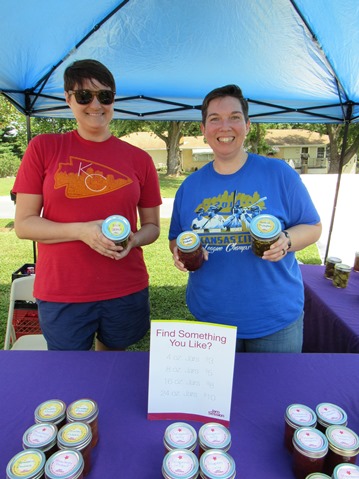 Michelle Ferguson and Kim Niebaum hold jars of dilly beans, holiday strawberry rhubarb jam and candied jalapenos at their booth at the Grinter Summerfest Saturday. Their enterprise is named "Jam Session. Teh two are in Johnson County, and  Niebaum is from Wyandotte County originally.  The  free Summerfest continue until 4 p.m. Saturday at 78th and K-32. (Staff photo)