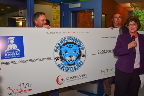 Brad Oliver, president of Catalyst Construction Group, presented a ceremonial check representing construction cost savings, to Kelli Mather, chief operating officer of the Kansas City, Kan., Public Schools.  The dedication ceremony of the new Frank Rushton Elementary School building took place on Sept. 13. (Photo by Brian Turrel)