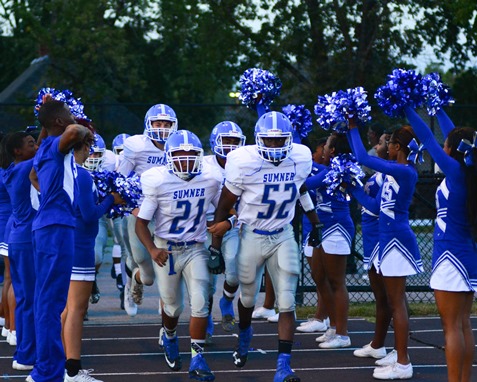 Sumner seniors Dominic Love (21) and Weah Landford (52) led their football team onto the field against Bishop Ward, encouraged by the Sumner cheerleaders. (Photo by Brian Turrel)