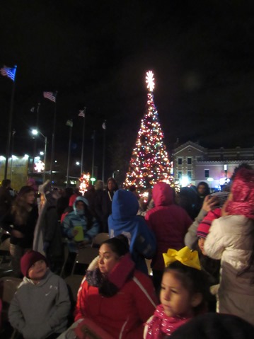 The Christmas tree in front of Kansas City, Kan., City Hall was lit on Friday night in a holiday ceremony. The crowd spent a lot of time indoors in the City Hall lobby with colder weather Friday. (Staff photo by Mary Rupert)